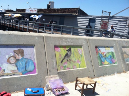 Three panels of chalk art on a wall near a pier
