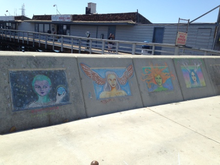 Four panels of chalk art on a wall near the ocean.