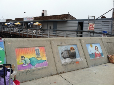 Chalk art in three panels, on a wall near a pier.